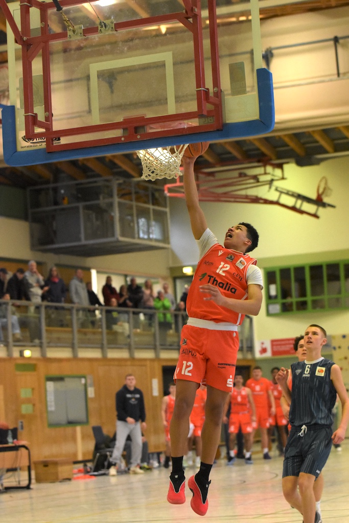 Ein Basketballspieler in orangem Trikot springt energisch zum Korbleger hoch