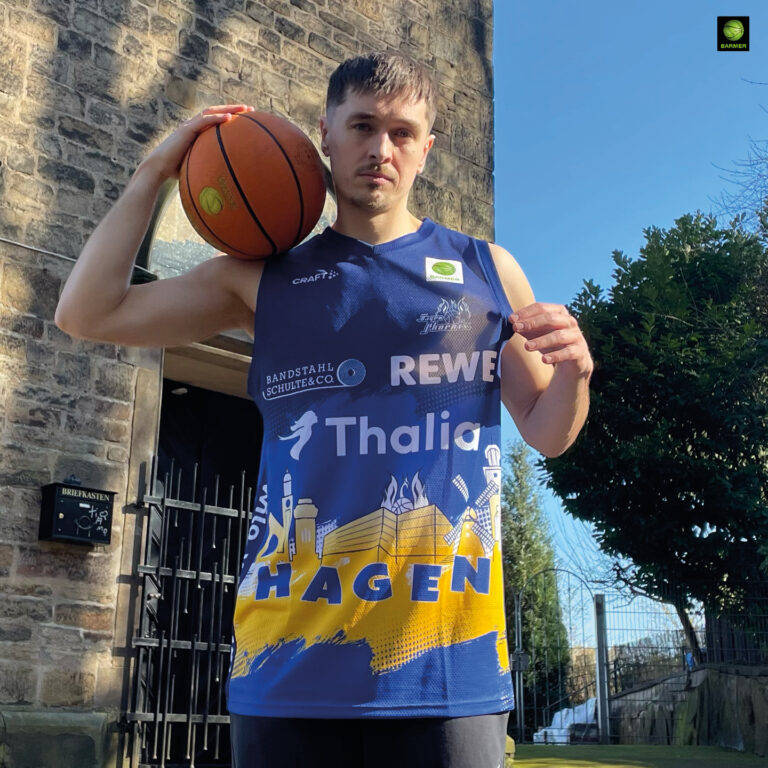 Junger Mann mit neutralem Blick hält Basketball und trägt blau gelbes Hagen Trikot