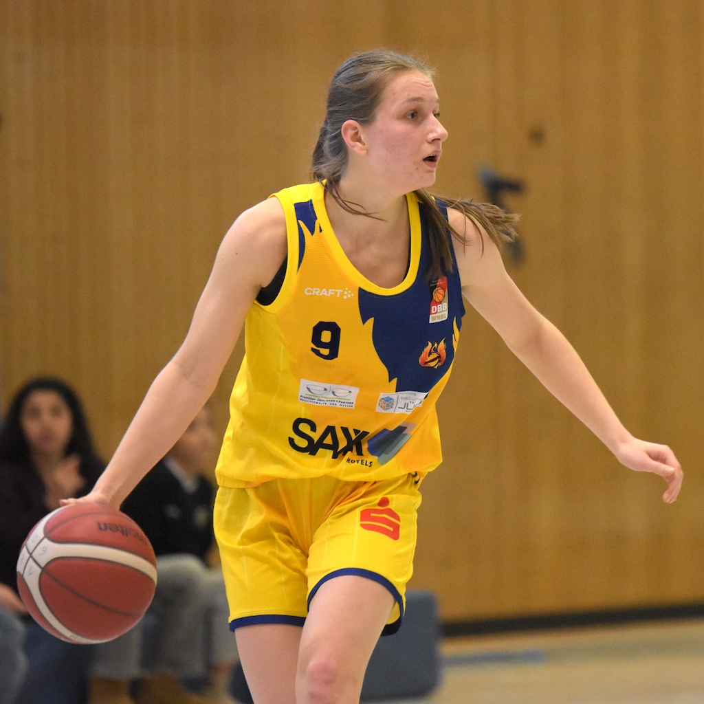 Eine junge Frau im gelben Basketballtrikot dribbelt konzentriert den Ball