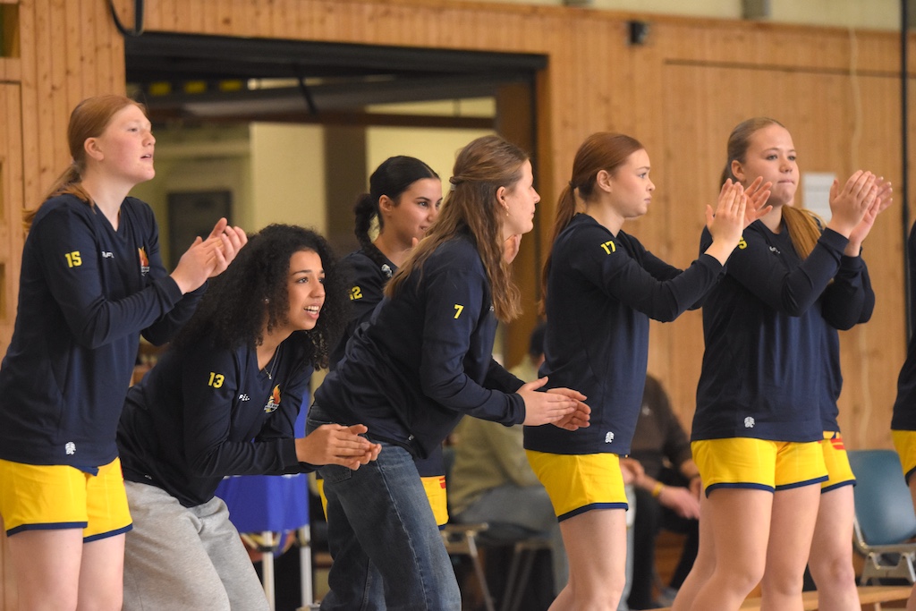 Sechs junge Frauen mit konzentrierten und erwartungsvollen Gesichtern klatschen motiviert, tragen dunkle Sporttrikots und gelbe Hosen