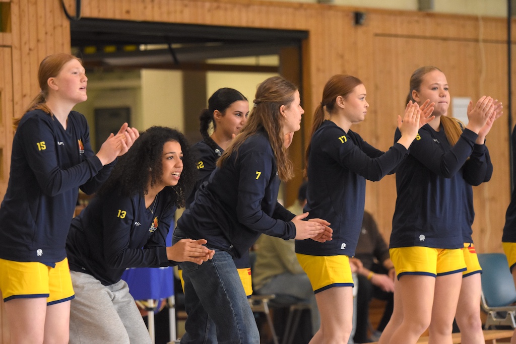 Sechs junge Frauen in dunkelblauen Trikots mit gelben Shorts klatschen und feuern motiviert an