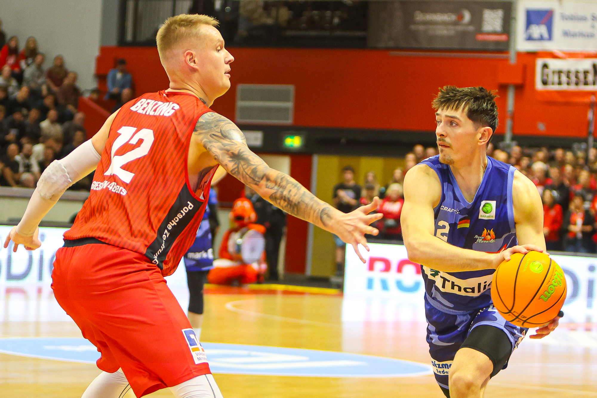 Zwei Basketballspieler im Spiel, einer in Rot verteidigt, der andere in Blau dribbelt entschlossen