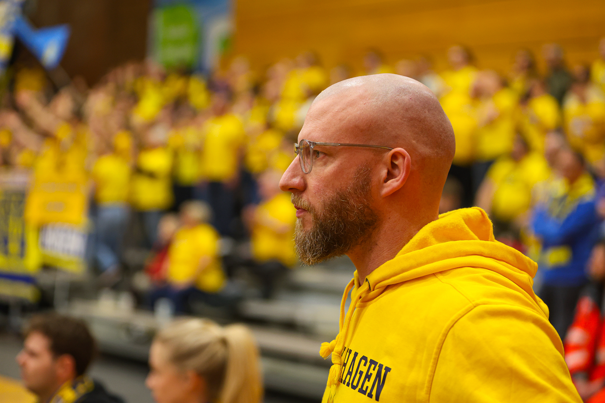 Ein bärtiger Mann mit Brille im gelben Hoodie blickt konzentriert in die Ferne