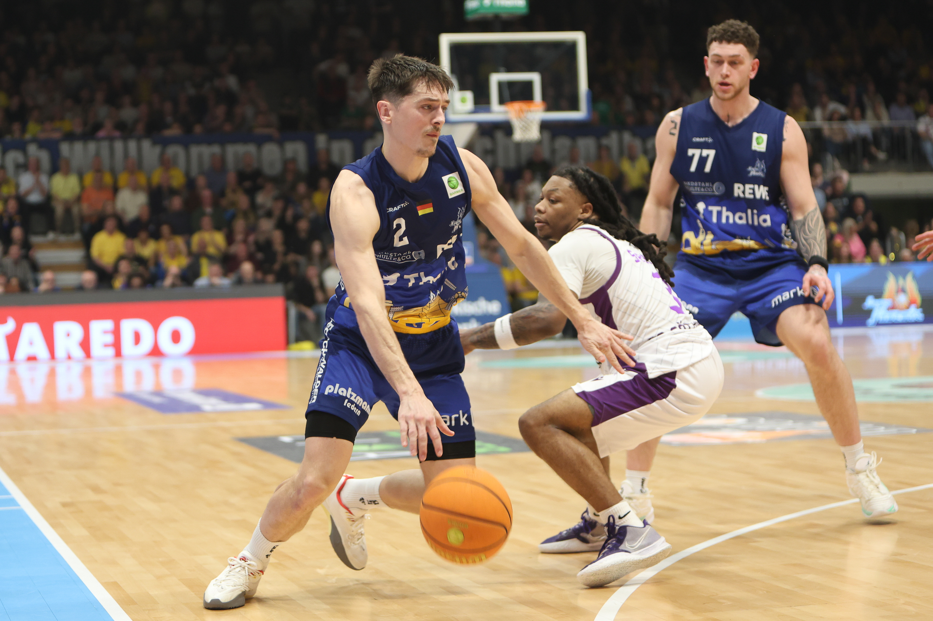 Ein Basketballspieler im blauen Trikot verteidigt konzentriert gegen einen Gegner in Weiß
