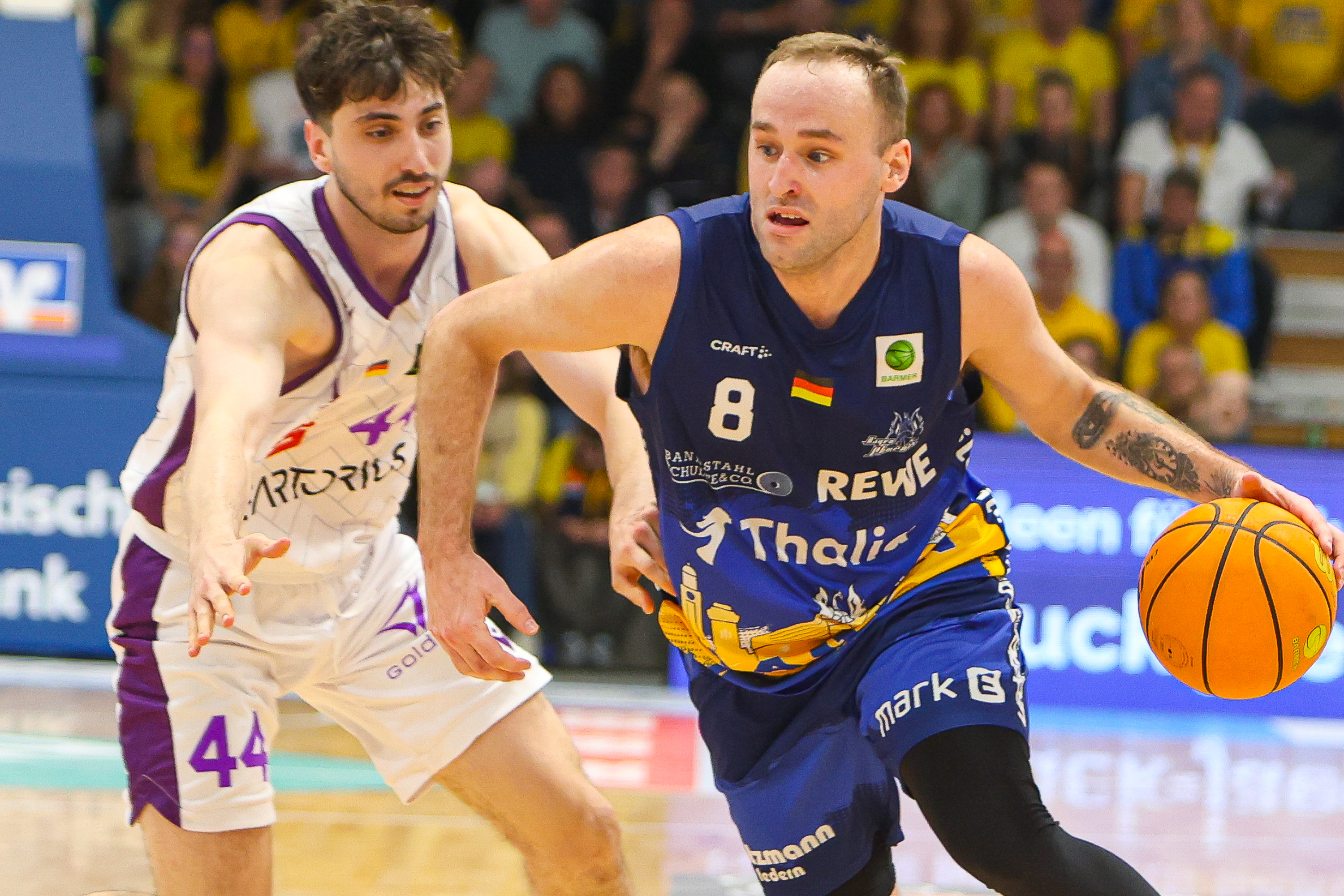 Ein Mann mit entschlossenem Blick dribbelt im blauen Trikot einen Basketball