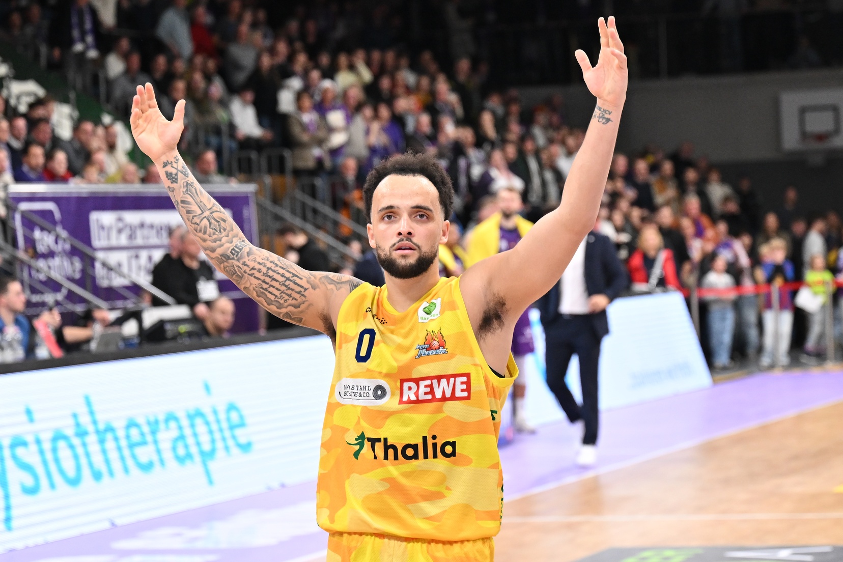 Ein Basketballspieler im gelben Trikot jubelt mit erhobenen Armen auf dem Spielfeld