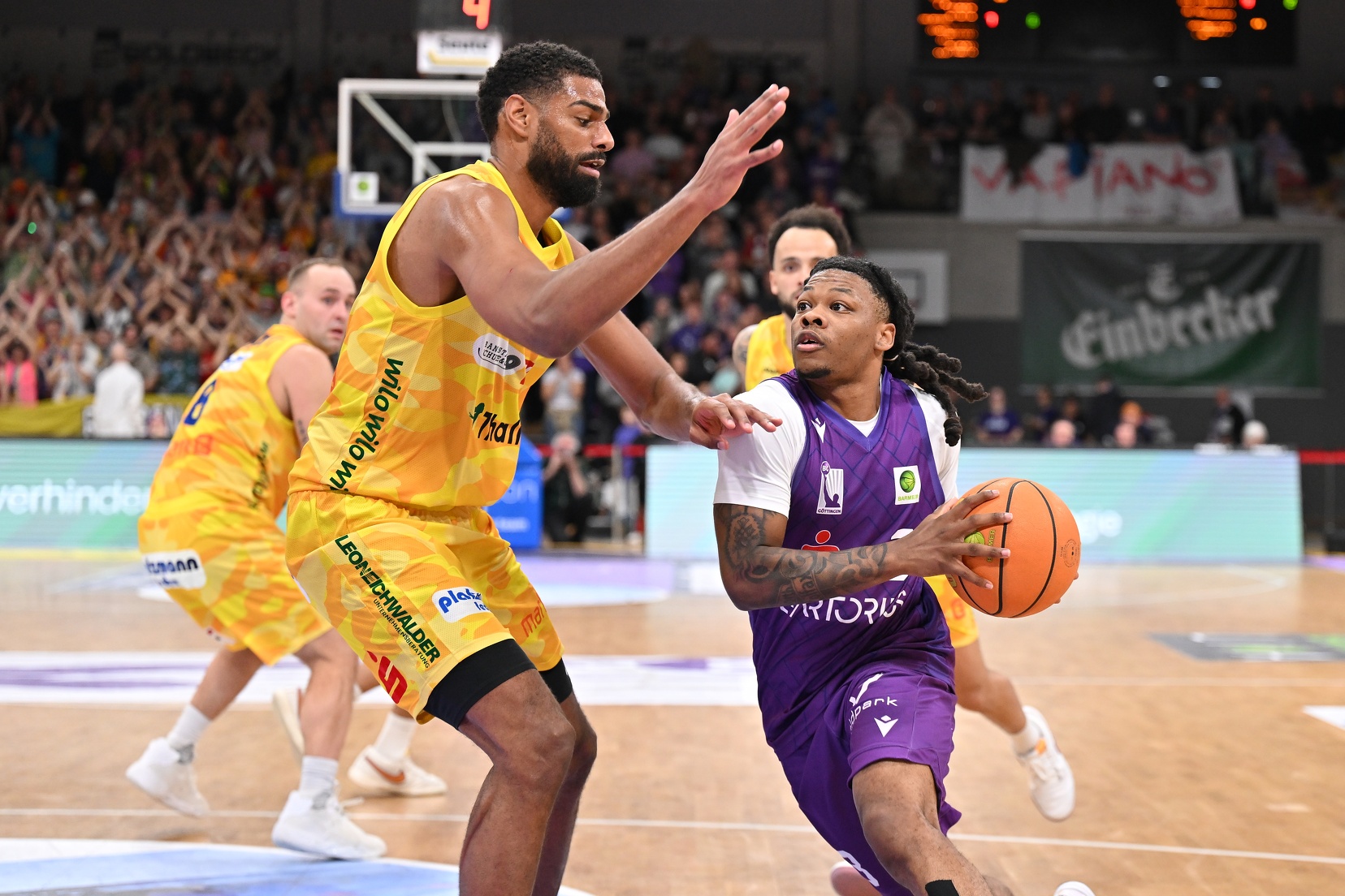 Zwei Basketballspieler im gelben und lila Trikot kämpfen konzentriert um den Ball