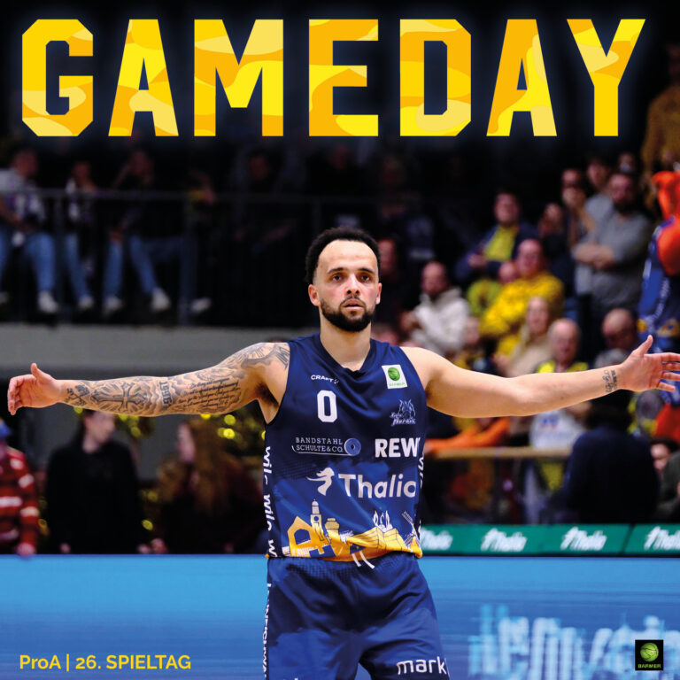 Ein Basketballspieler in dunkelblauem Trikot steht mit ausgebreiteten Armen auf dem Spielfeld