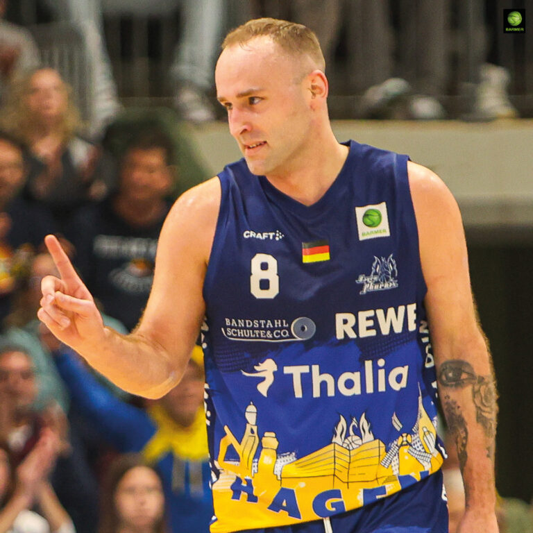 Ein Basketballspieler in blau-gelbem Trikot macht ein Victory-Zeichen und lächelt leicht