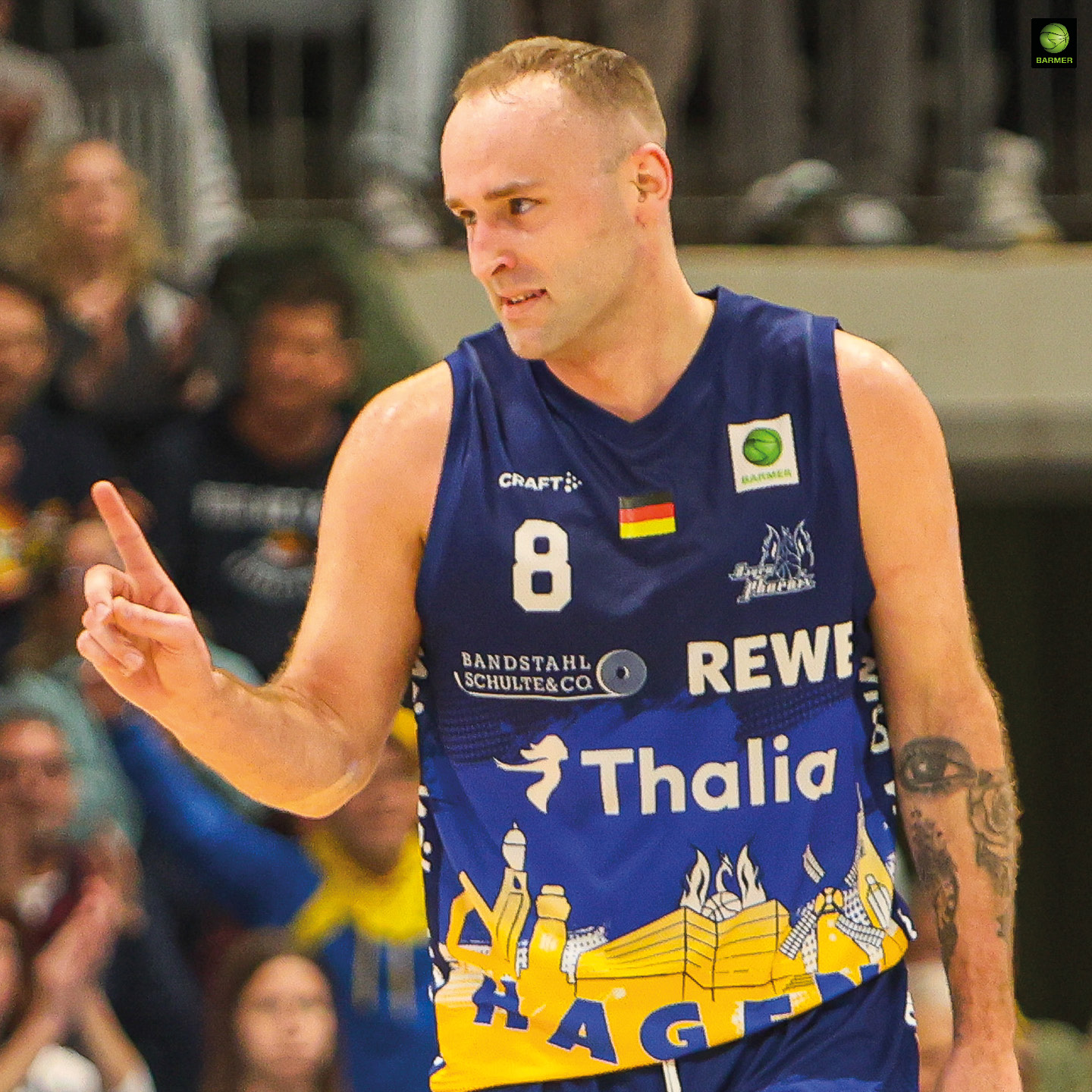 Ein Basketballspieler in blau-gelbem Trikot macht ein Victory-Zeichen und lächelt leicht