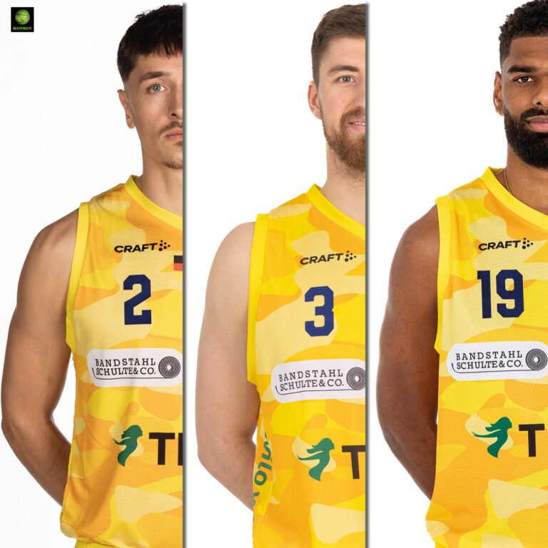 Drei männliche Basketballspieler in gelben Trikots schauen ernst in die Kamera