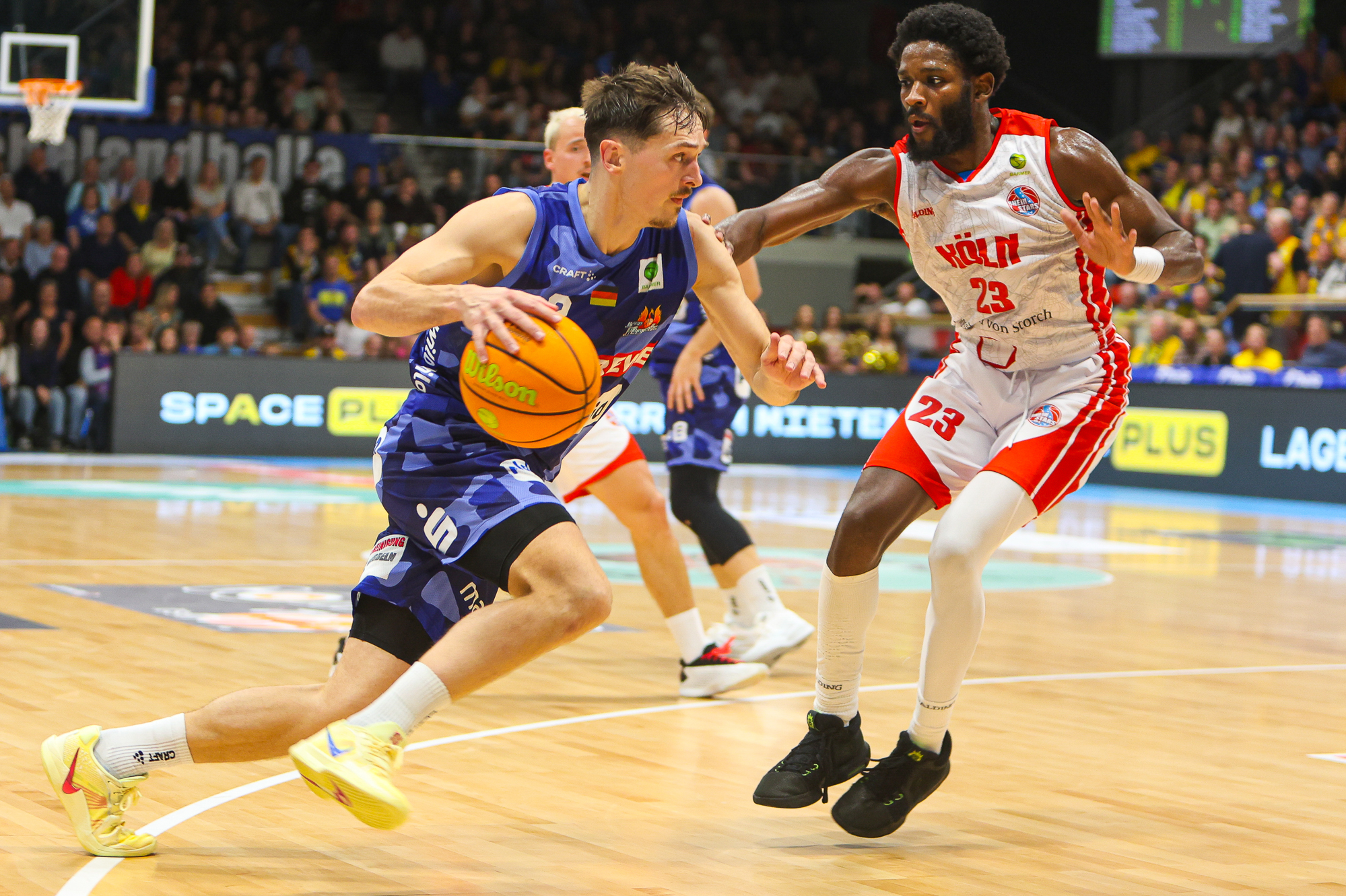 Ein Basketballspieler im blauen Trikot dribbelt konzentriert am Gegner vorbei