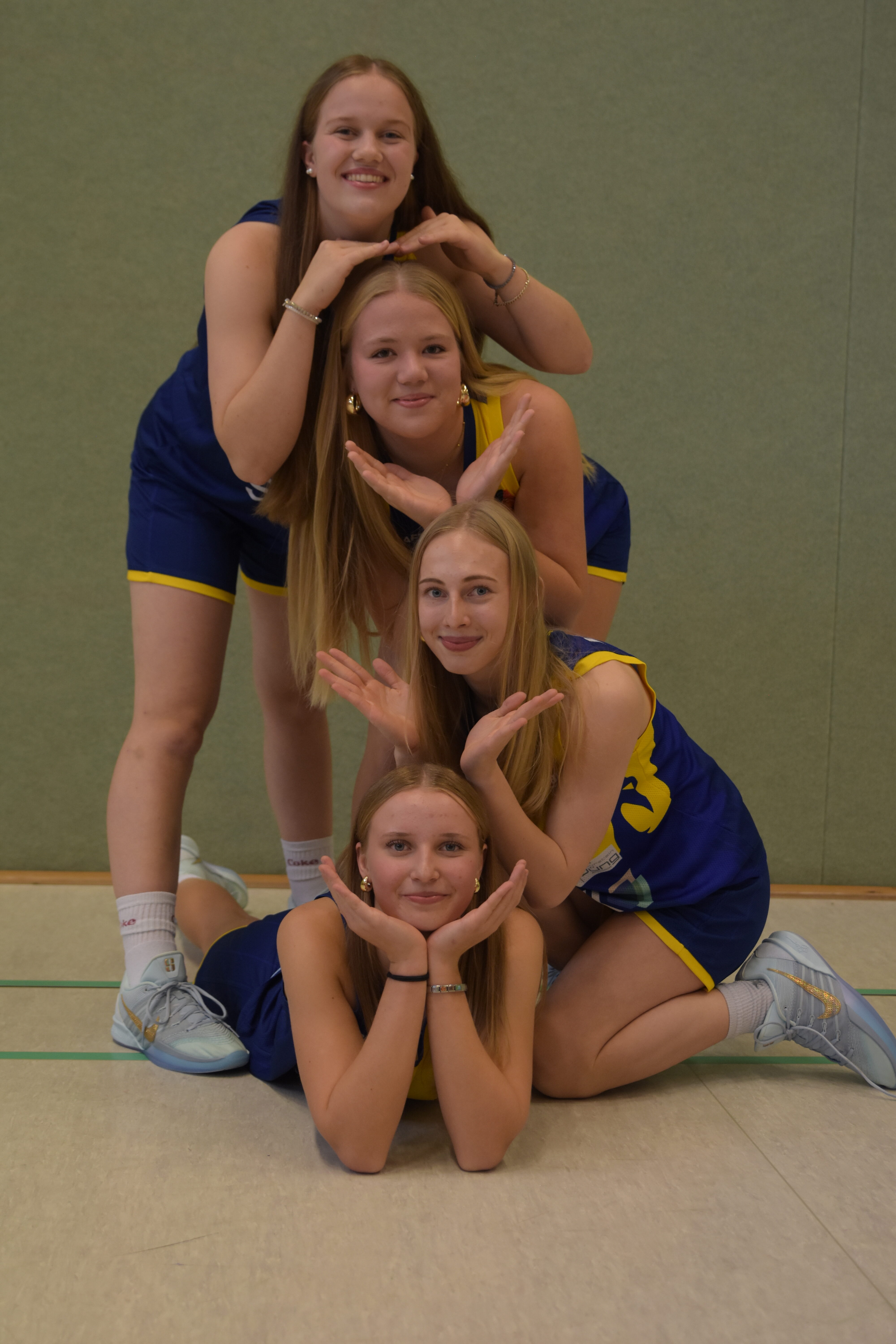 Vier junge Frauen im blauen Sportoutfit posieren lächelnd in einer Pyramidenform