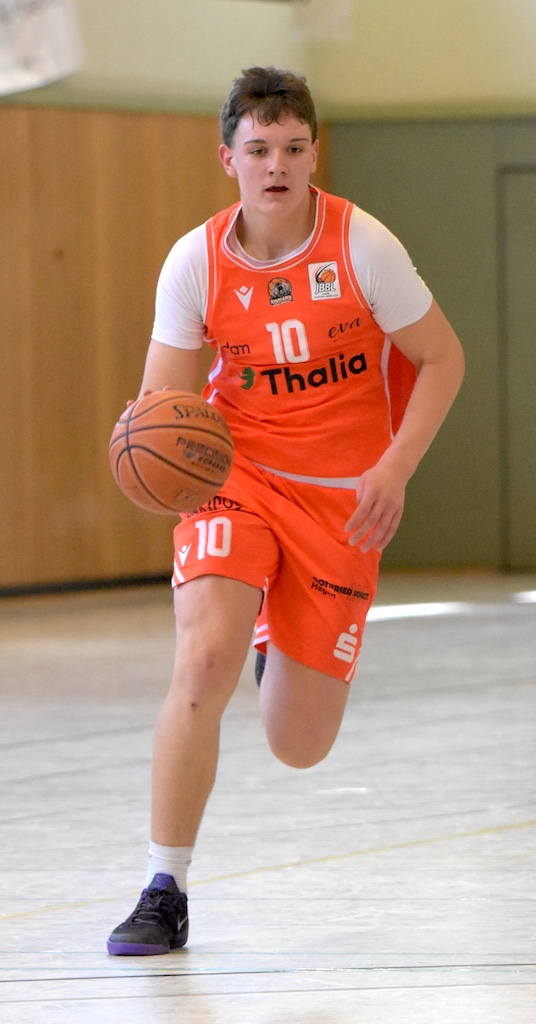 Junger Basketballspieler im orangefarbenen Trikot mit konzentriertem Blick beim Dribbeln