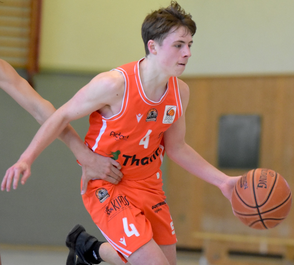 Ein junger Basketballspieler im orangefarbenen Trikot dribbelt fokussiert den Ball