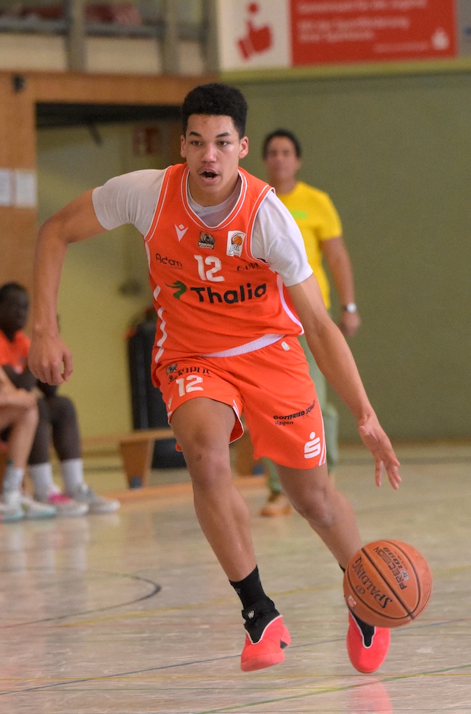 Ein junger Basketballspieler im orangefarbenen Trikot dribbelt konzentriert den Ball