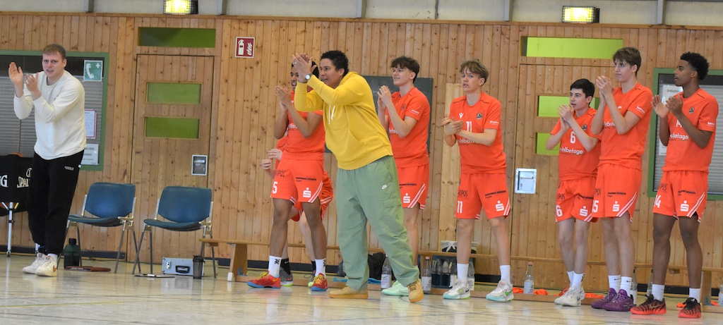 Eine Gruppe junger Männer im orangefarbenen Trikot applaudiert und wirkt begeistert