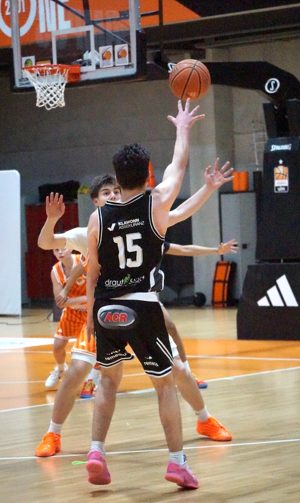 Zwei junge Basketballspieler in schwarzen und orangefarbenen Trikots im Spielmoment