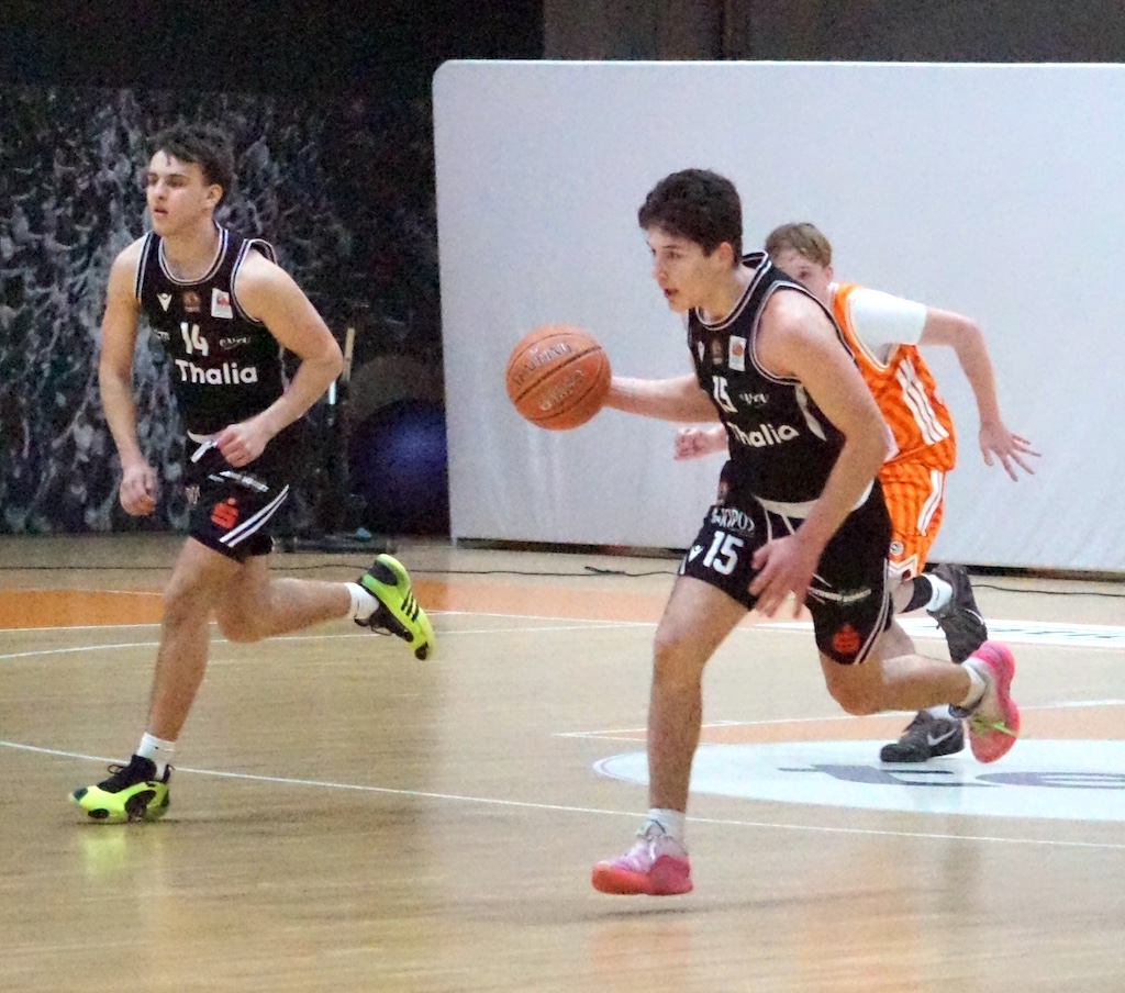 Ein junger Basketballspieler im schwarzen Trikot dribbelt konzentriert den Ball auf dem Spielfeld