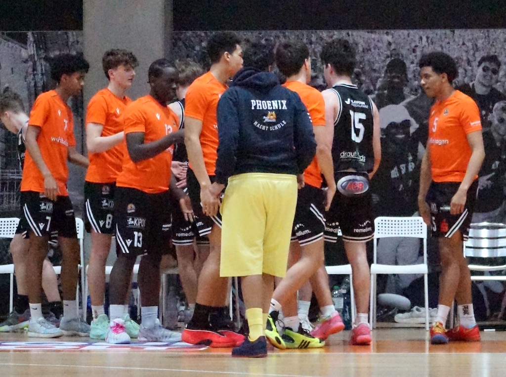Eine Basketballmannschaft mit orangefarbenen Trikots berät sich lebhaft am Spielfeldrand