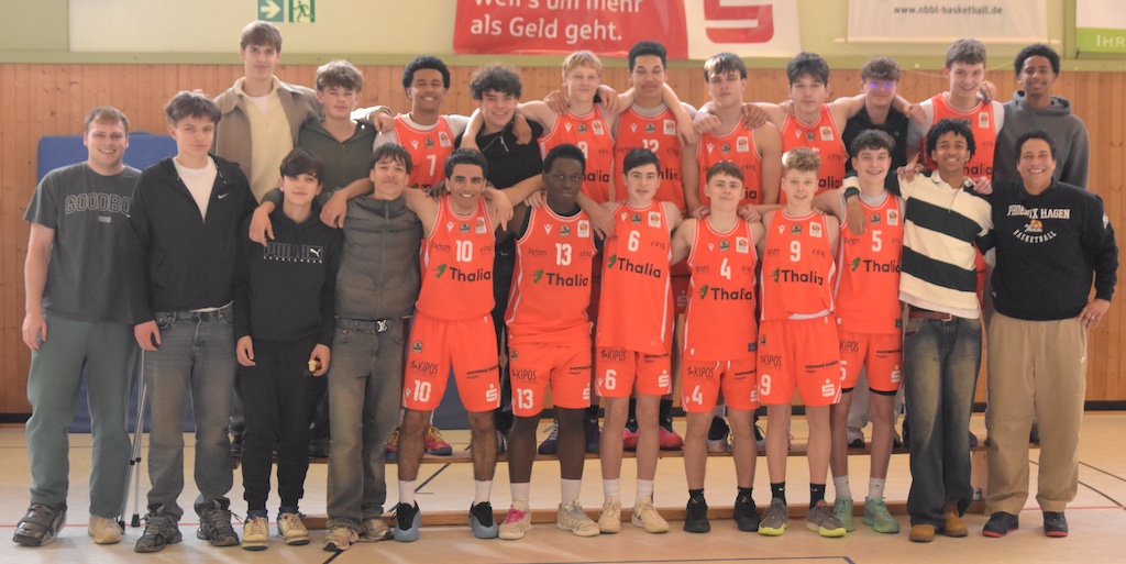 Eine männliche Basketballmannschaft in auffällig orangen Trikots lächelt in der Turnhalle
