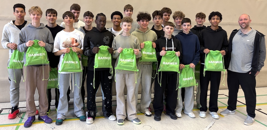 Eine Gruppe Jugendlicher und ein Erwachsener lächeln und halten grüne BARMER Turnbeutel