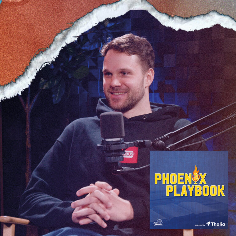 Ein Mann mit braunen Haaren lächelt entspannt im Podcaststudio vor Mikrofonen