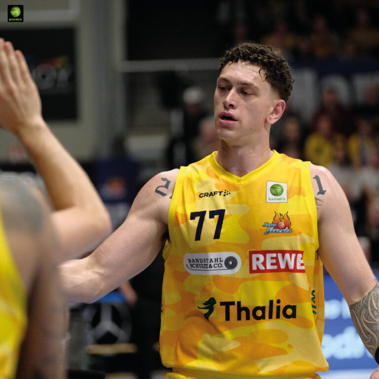 Ein Basketballspieler im gelben Trikot klatscht mit ruhigem Gesichtsausdruck ab