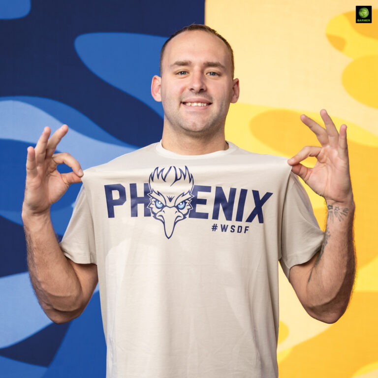 Ein lächelnder Mann zeigt sein helles PHOENIX Shirt vor buntem Hintergrund