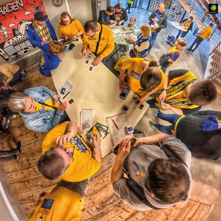 Menschen in gelber Kleidung tauschen fröhlich Sammelbilder an einem weißen Tisch