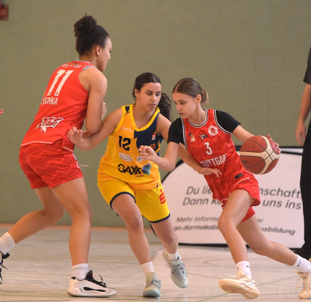 Drei Basketballspielerinnen im Spiel, eine mit konzentriertem Blick führt den Ball