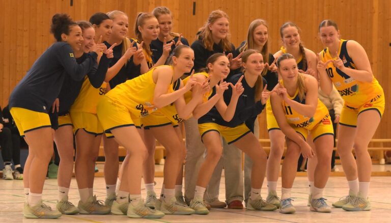 Eine Frauen-Basketballmannschaft in gelben Trikots posiert lachend und freundlich