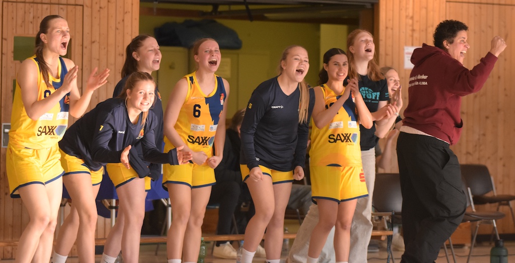 Eine Gruppe junger Frauen im gelben Basketballtrikot jubelt begeistert am Spielfeldrand