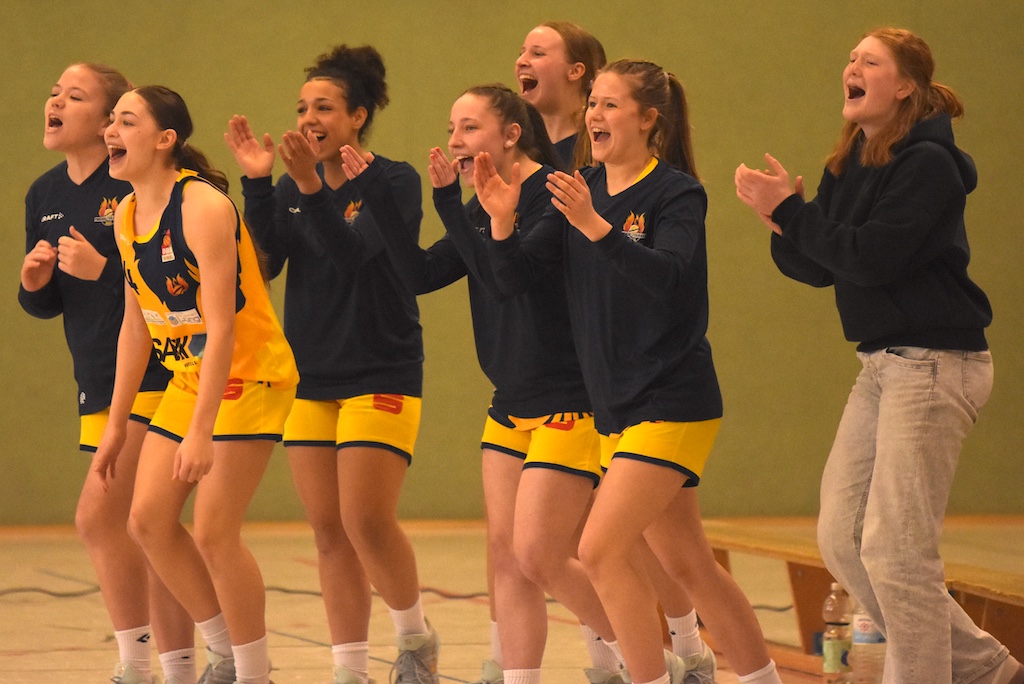 Sechs junge Frauen jubeln lachend und klatschend im gelb-blauen Sportoutfit
