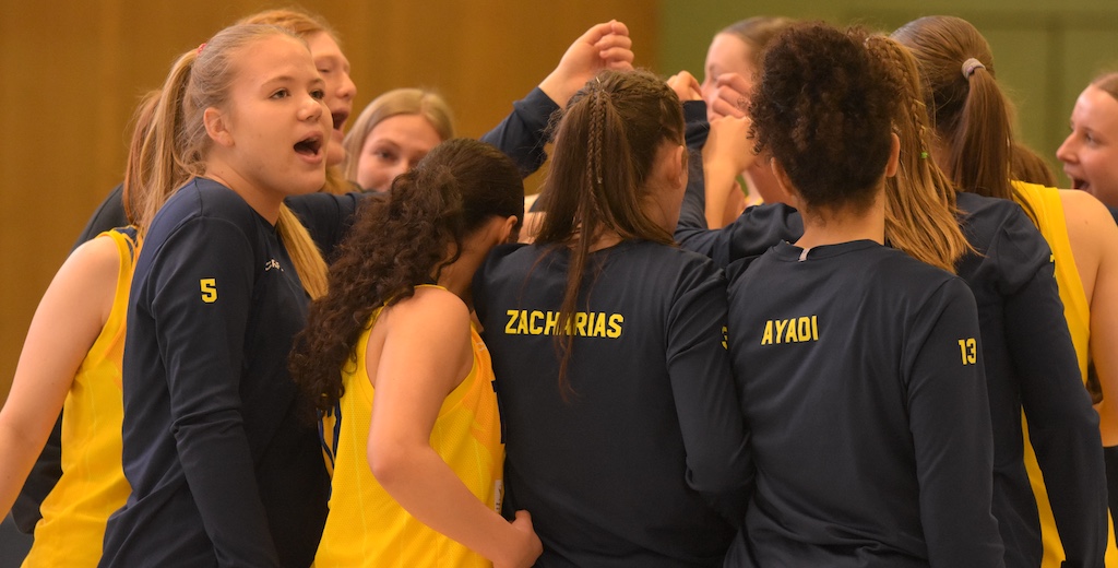 Mehrere junge Frauen im gelb-blauen Sportoutfit jubeln motiviert im Kreis