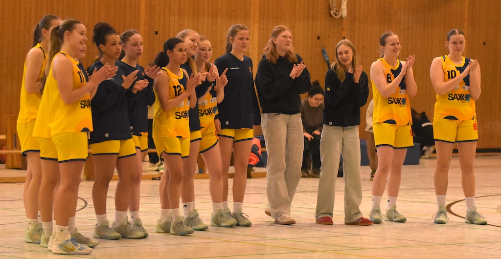 Eine Gruppe junger Basketballspielerinnen in gelben Trikots applaudiert lächelnd