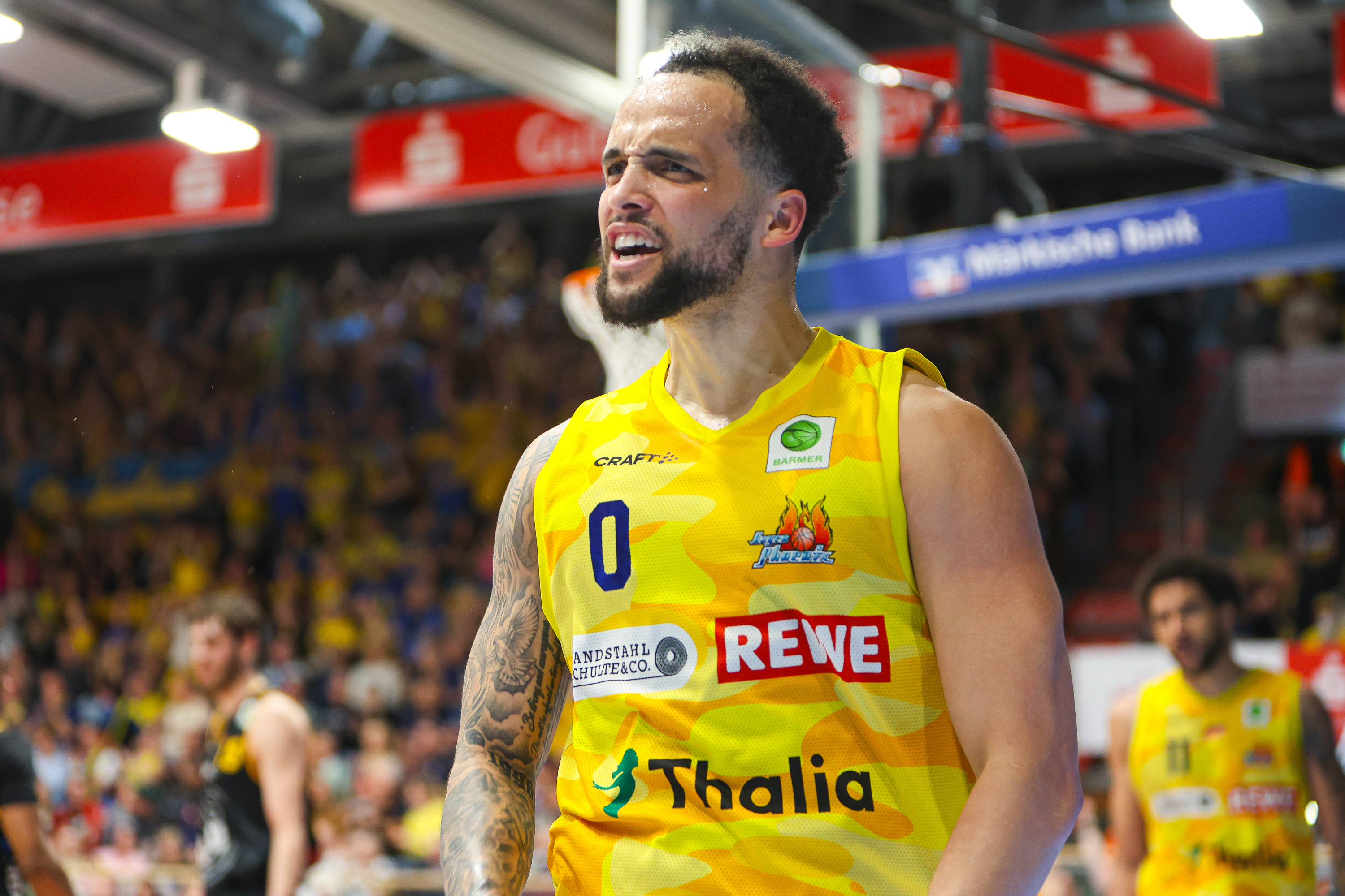 Ein Basketballspieler im gelben Trikot mit ernster Miene und tätowiertem Arm