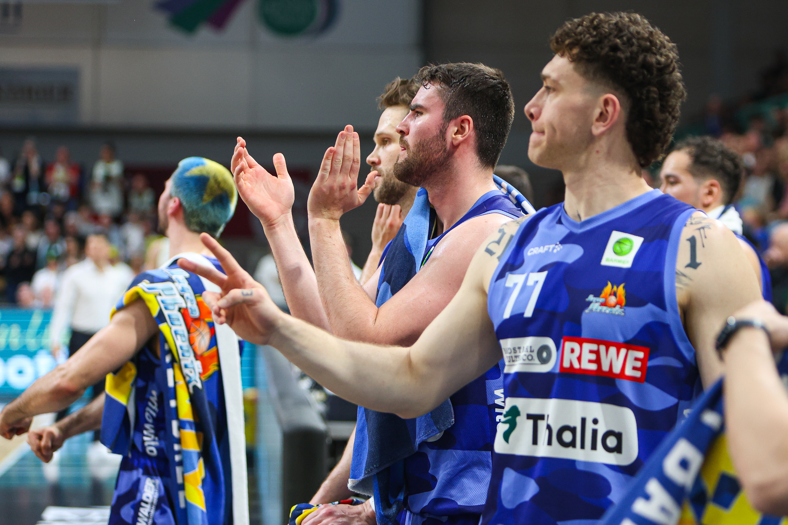 Vier Basketballspieler im blauen Trikot jubeln am Spielfeldrand und wirken begeistert