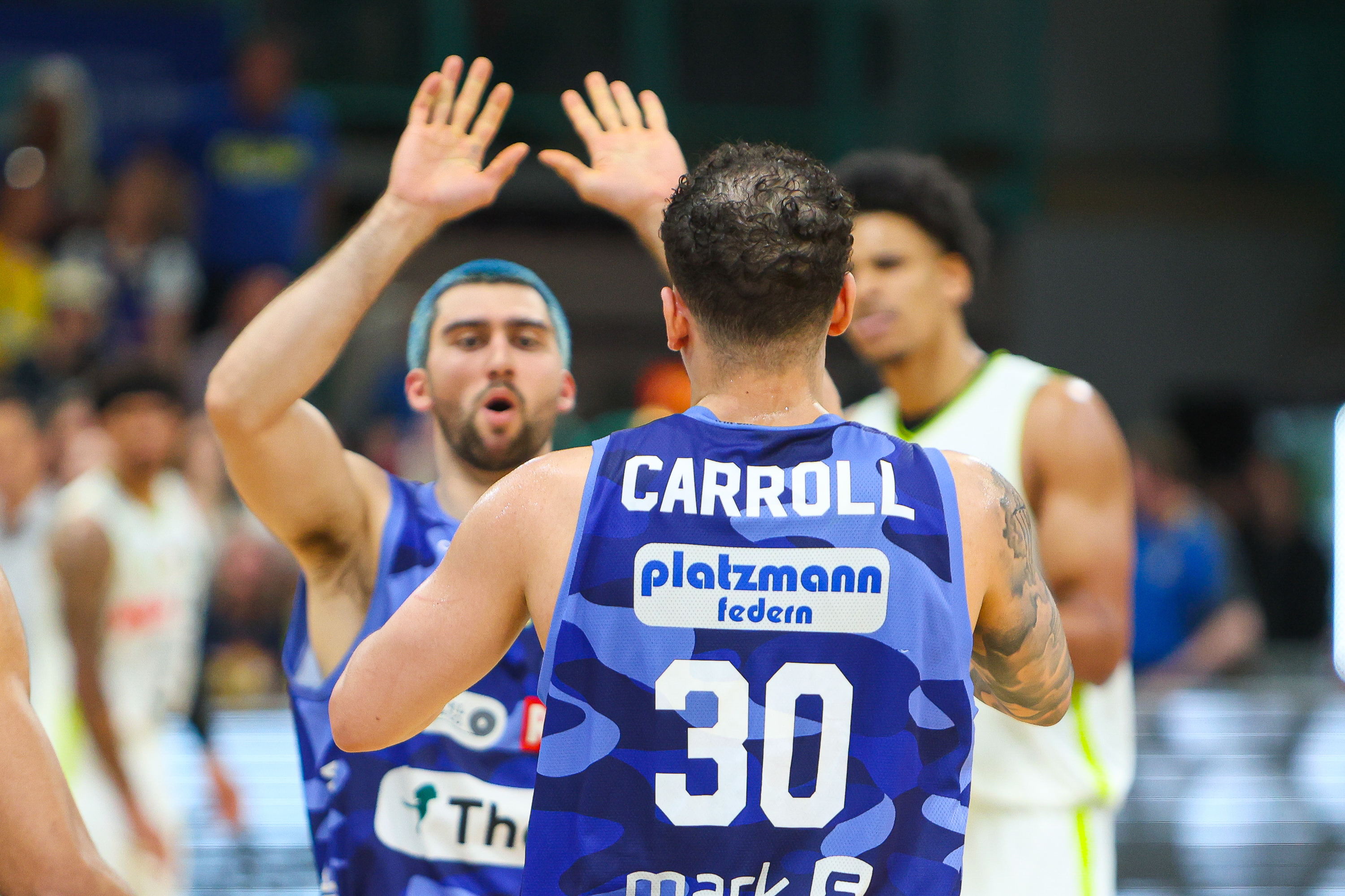 Zwei Basketballspieler in blauen Trikots jubeln, einer trägt den Namen Carroll und Nummer 30