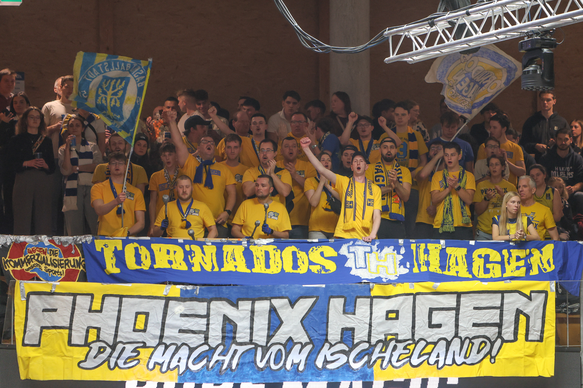 Eine Gruppe begeisterter Phoenix Hagen Fans in gelben Shirts jubelt lebhaft mit Fahnen