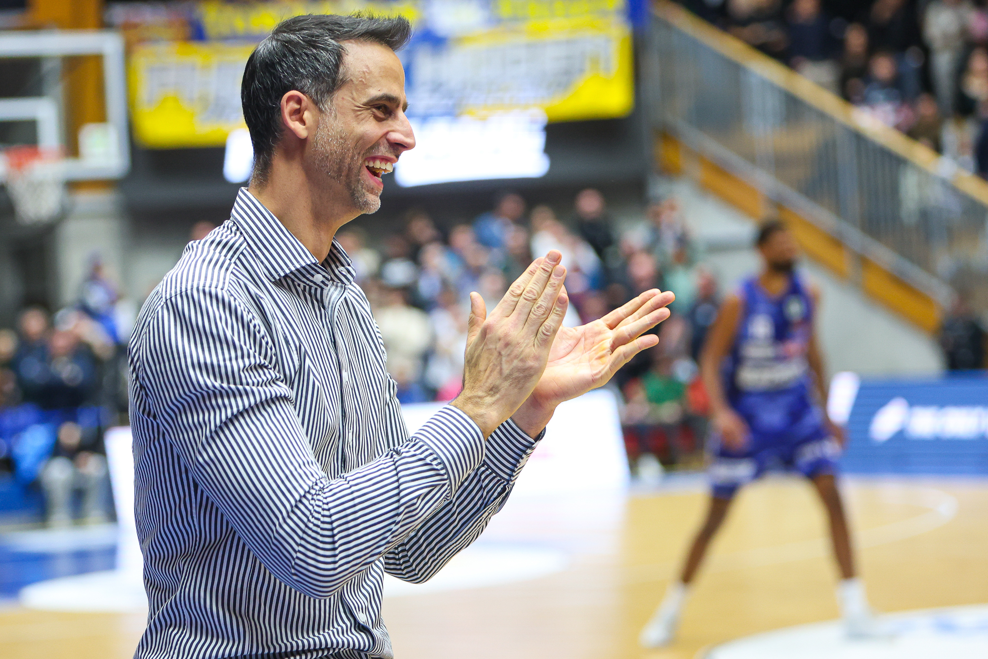 Ein Mann mit gestreiftem Hemd lacht herzlich und klatscht begeistert in der Halle
