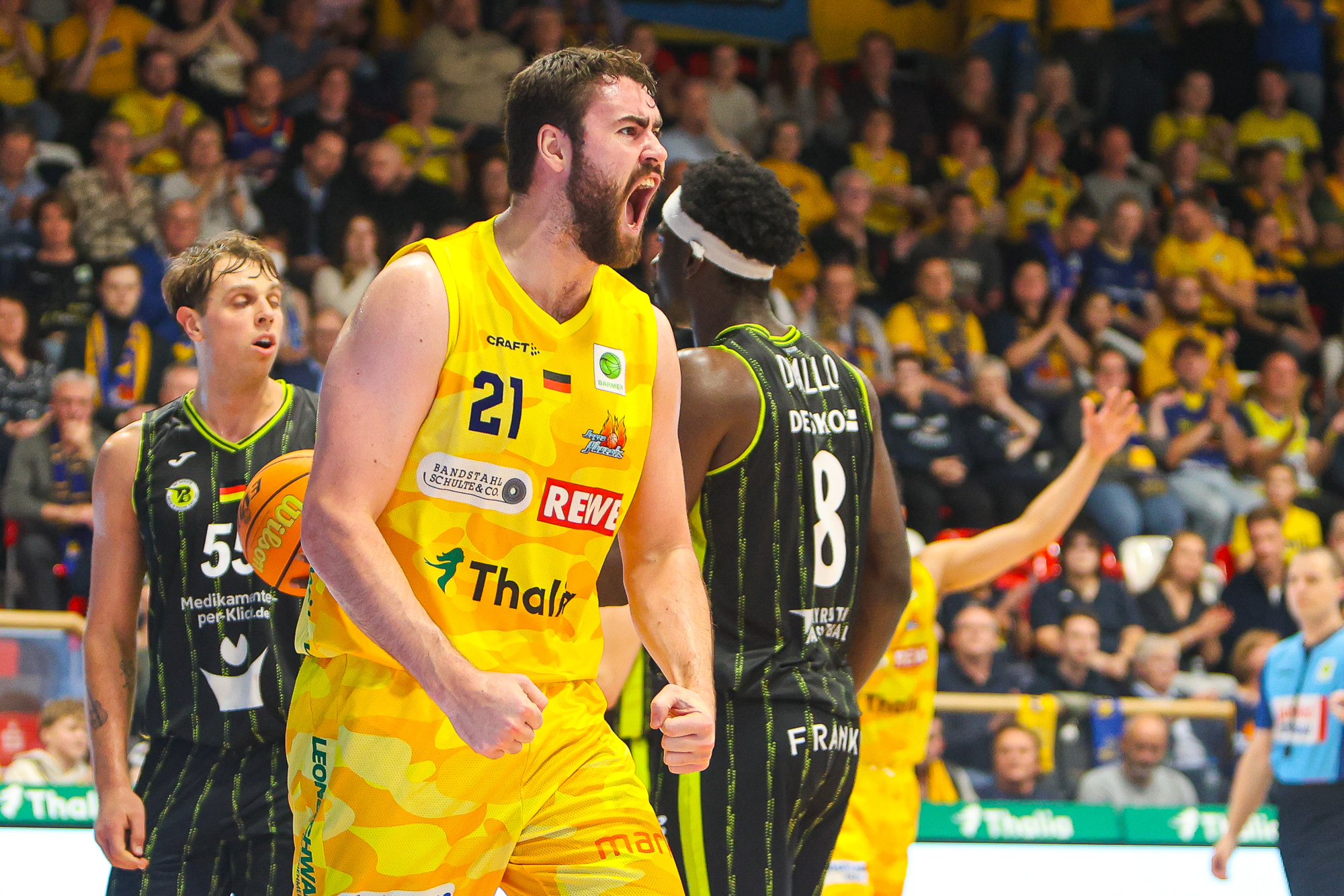 Ein bärtiger Basketballspieler im gelben Trikot jubelt lautstark vor begeistertem Publikum