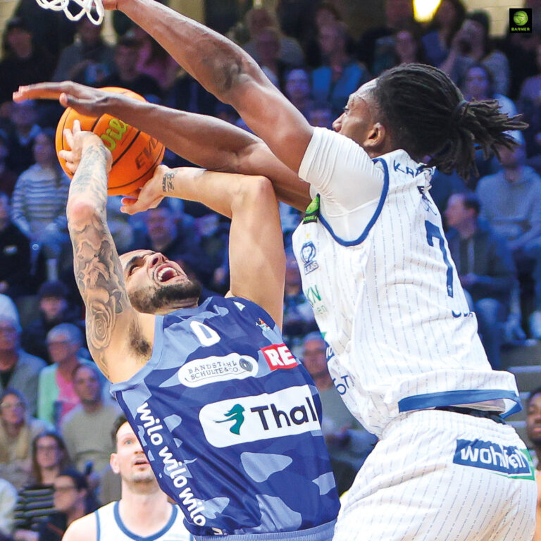 Zwei Basketballspieler kämpfen energisch am Korb, einer blockt den Wurf des anderen