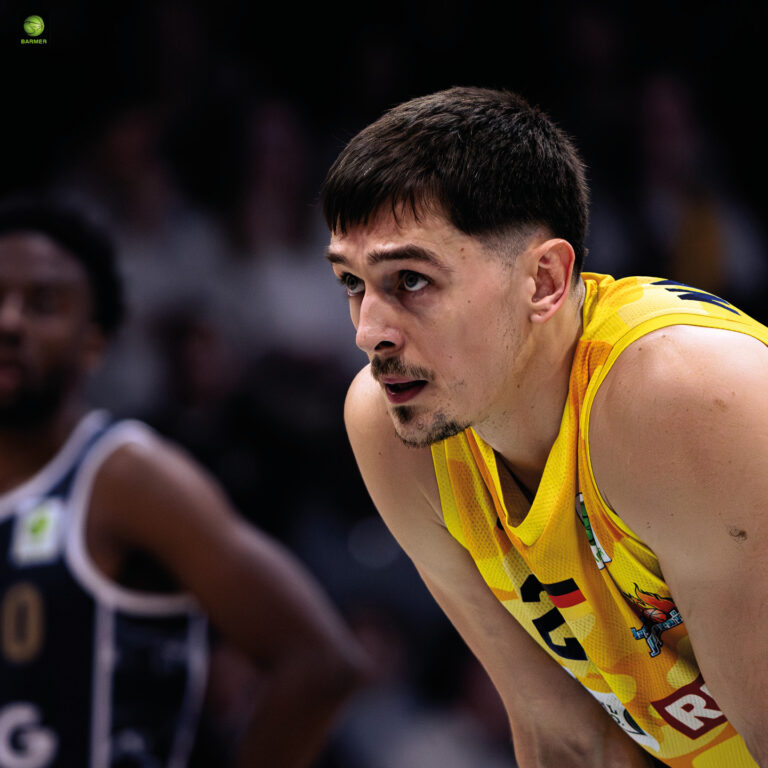 Ein Basketballspieler im gelben Trikot schaut konzentriert nach vorne, dunkle Haare