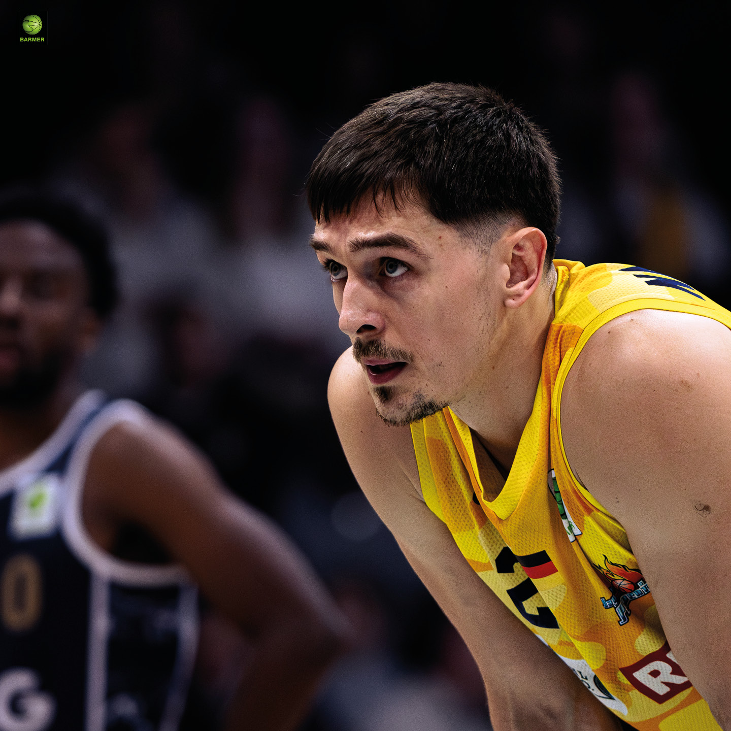 Ein Basketballspieler im gelben Trikot schaut konzentriert nach vorne, dunkle Haare