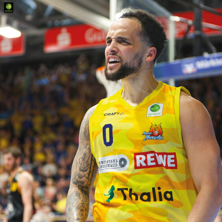 Ein Basketballspieler im gelben Trikot jubelt leidenschaftlich und schaut entschlossen