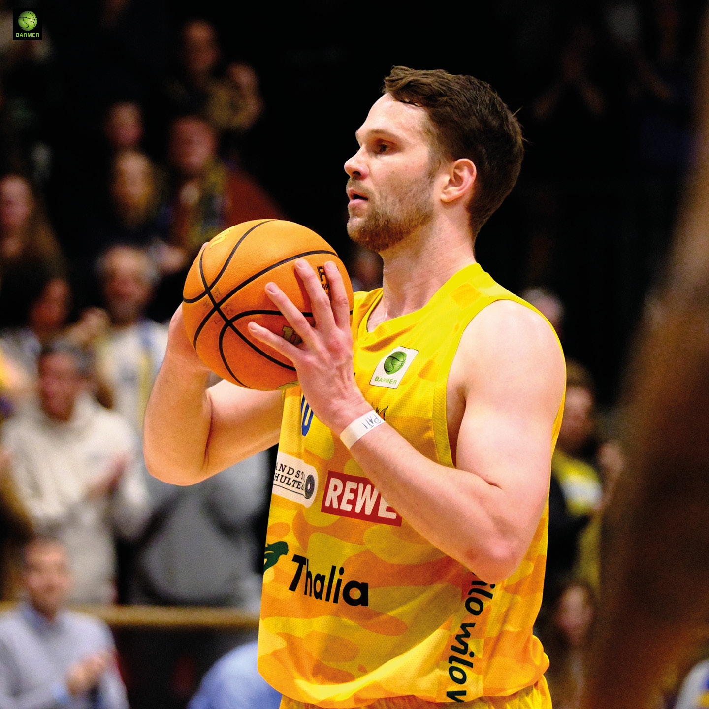 Ein konzentrierter Basketballspieler im gelben Trikot hält einen orangefarbenen Ball