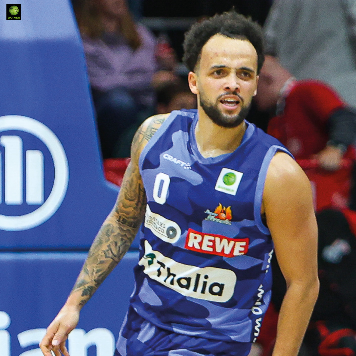 Ein Basketballspieler mit dunklen Locken schaut konzentriert zur Seite im blauen Trikot