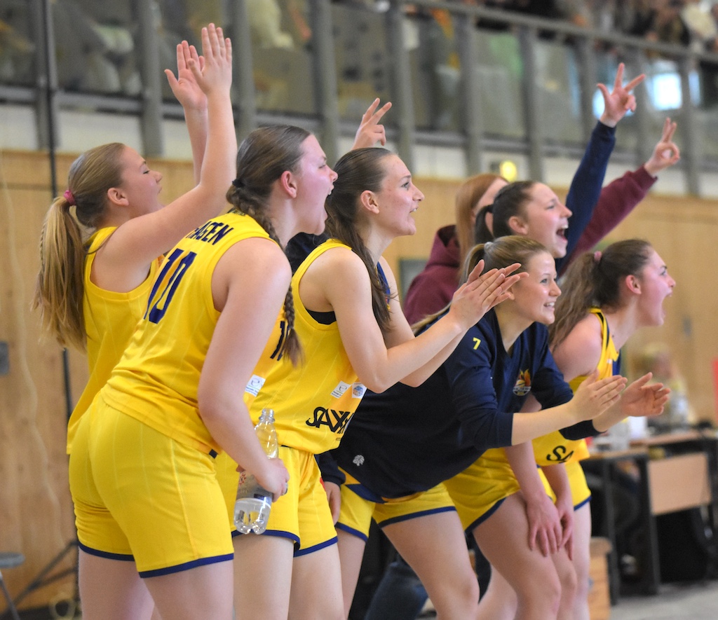 Eine Gruppe junger Frauen im gelben Basketballtrikot jubelt und gestikuliert freudig