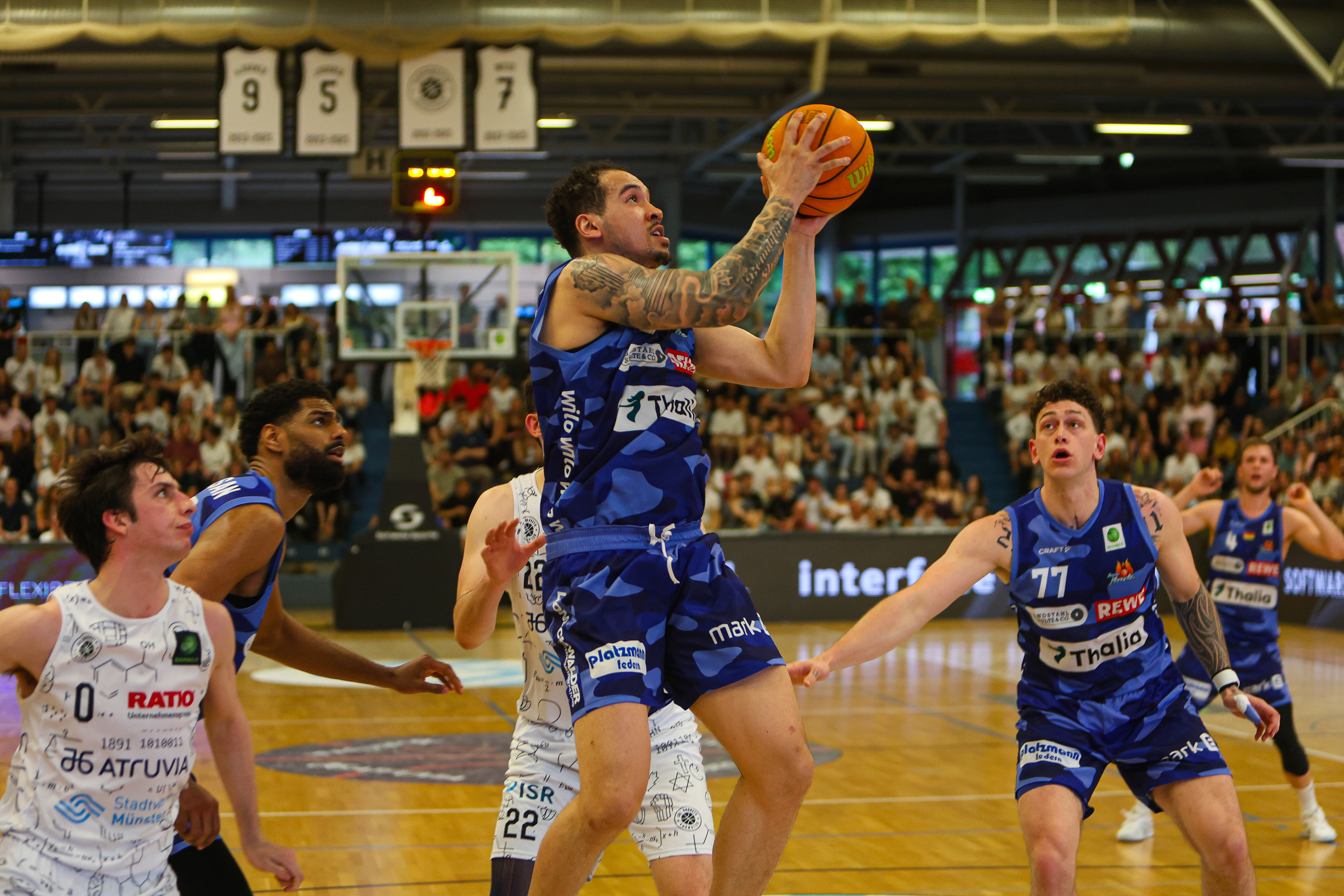 Ein Basketballspieler im blauen Trikot springt zum Korb, konzentriert und entschlossen